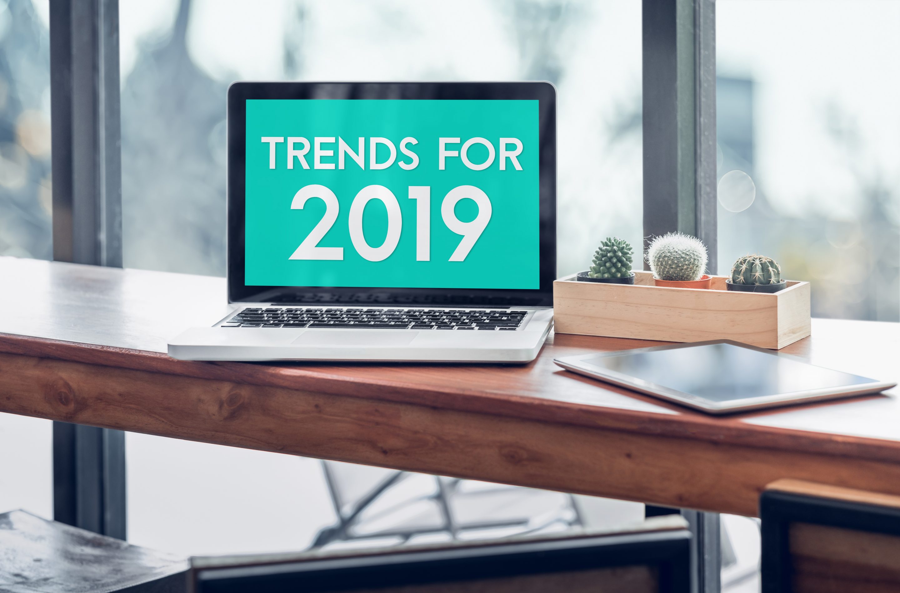 Trends for 2019 word in laptop computer screen with tablet on wood stood table in at window with blur background,Digital Business or marketing trending