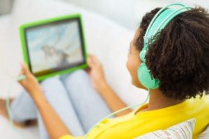 close up of happy african american young woman lying with tablet pc computer and headphones listening to music and watching video at home