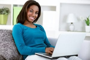 Young girl with laptop computer, sitting in bright living room, looking at camera.