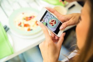 Portrait of a woman making photo of food on smartphone in restaurant