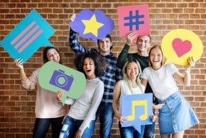 group of happy young adults holding graphic signs indicating the importance of engaging with audiences for social media marketing branding.