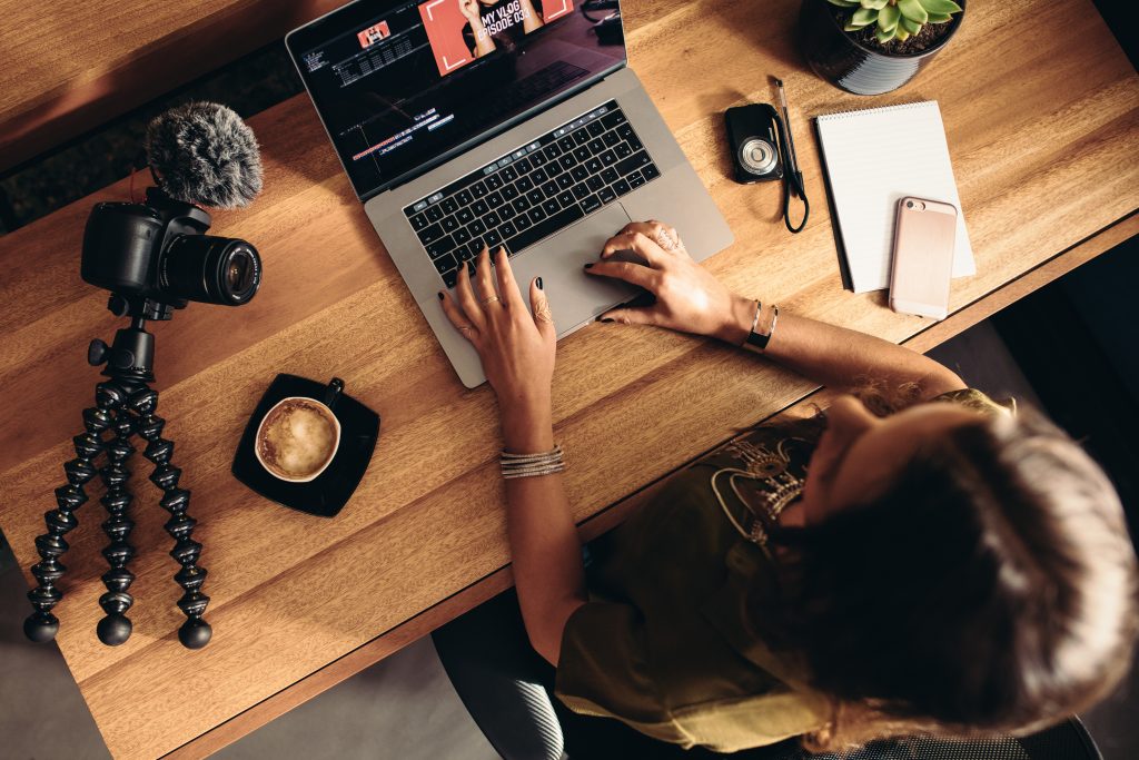 A woman editing a video on a laptop with a camera next to her 