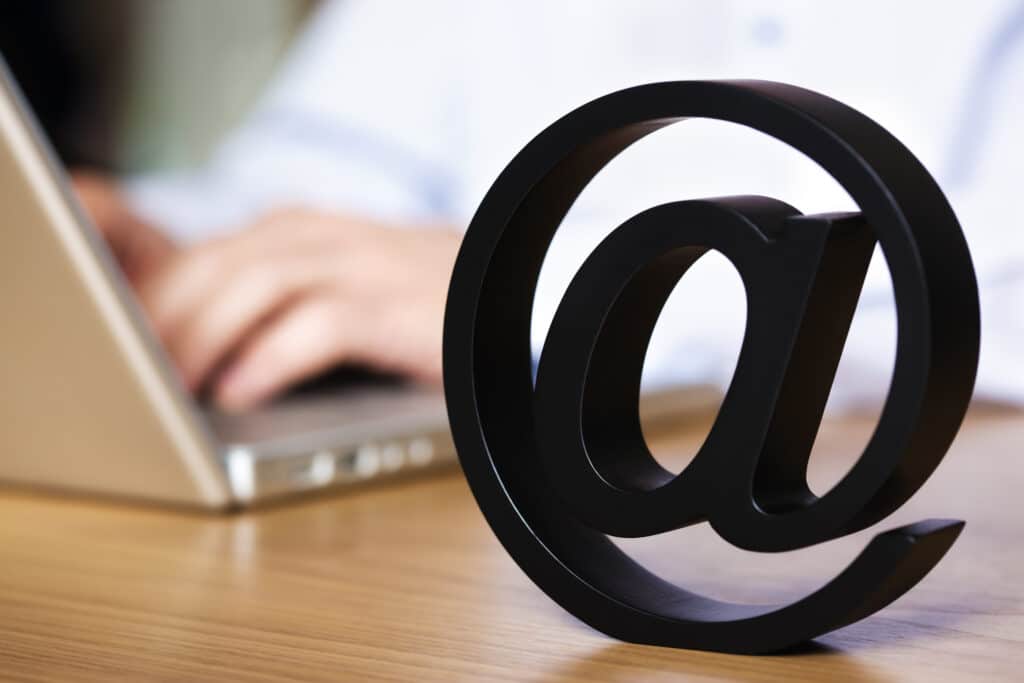 Person sitting at a desk typing on a laptop with an @ symbol.