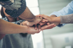 A group of people stacking hands together in a gesture of teamwork and unity, viewed from below.